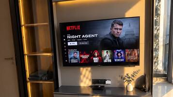 Una sala de estar moderna con un televisor de pantalla plana grande montado en la pared, una estantería empotrada y una cama con una manta texturizada.