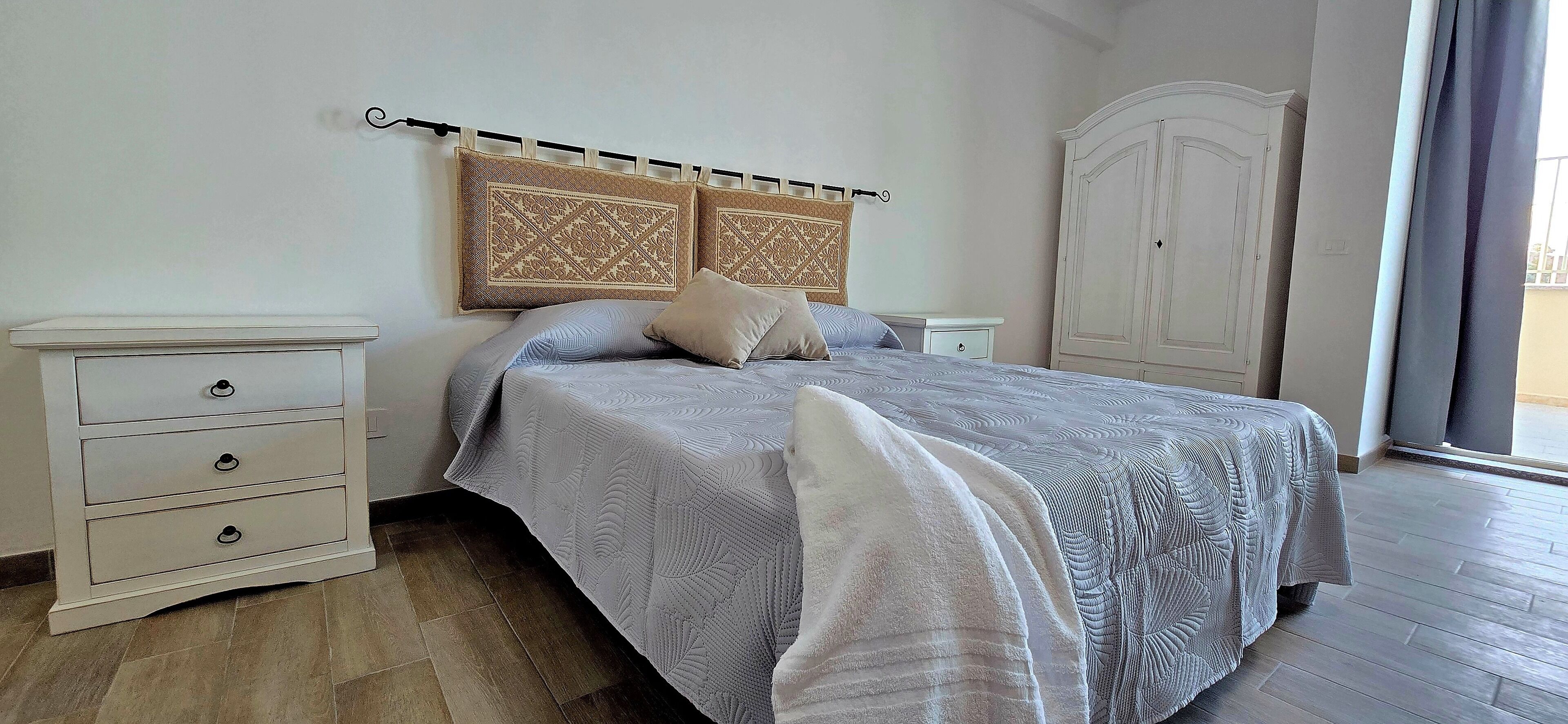 A bedroom with a bed, a nightstand, a wardrobe, and a window with curtains.