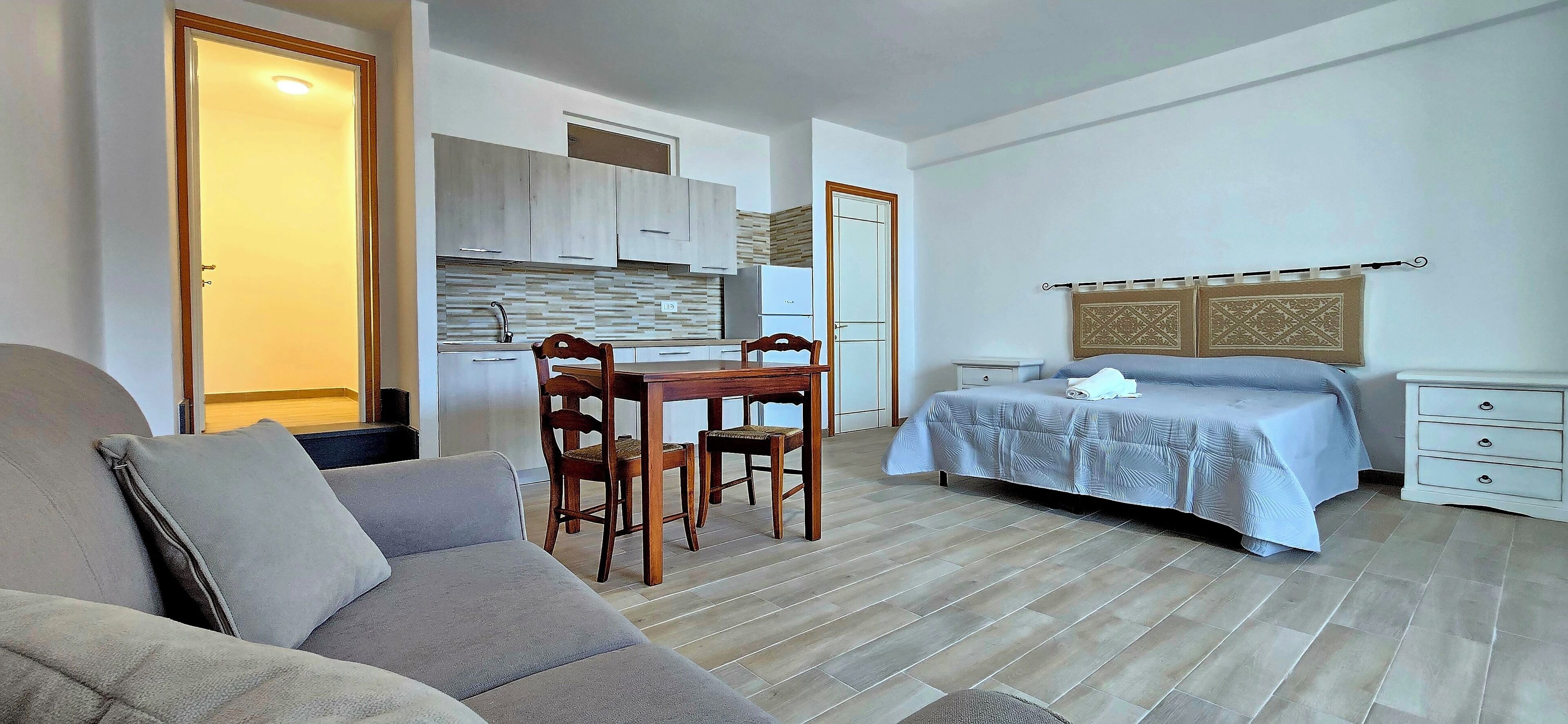 Quarto compacto com cozinha americana, sala de jantar com mesa e cadeiras, cama com cabeceira e sofá.