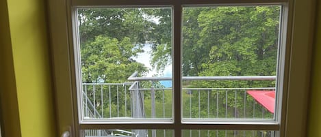 A room with a large window offering a view of a balcony with a red awning and metal railings.