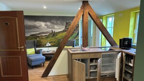 Une pièce comprenant un bureau en bois, une chaise, un canapé, une machine à café et une fresque représentant un paysage montagneux.