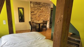 Une chambre avec un lit, une table à manger avec des chaises, un mur en pierre et un escalier.