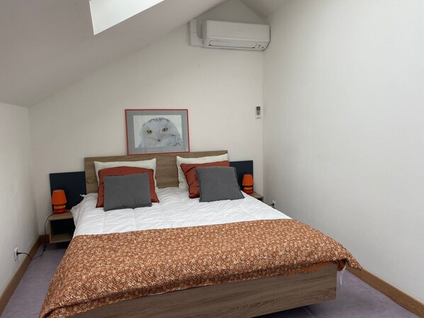 A bedroom with a bed, a framed owl picture, an air conditioner, and bedside lamps.