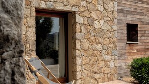 Eine Steinsichtmauer, ein Holzterrasse und ein Fenster mit Blick.