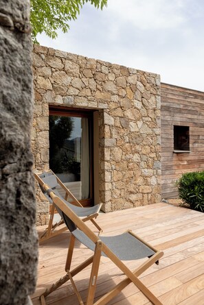 Eine Steinsichtmauer, ein Holzterrasse und ein Fenster mit Blick.