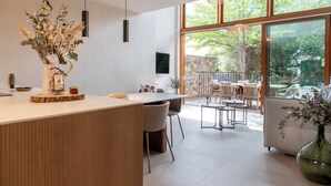 Een moderne keuken met een centraal eiland, een eetgedeelte met stoelen en grote ramen met uitzicht op de omgeving.