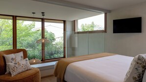 Een slaapkamer met een groot raam, een bed, een stoel en een televisie aan de muur.