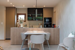 Une cuisine moderne avec un îlot central, deux chaises, un vase de fleurs et un luminaire suspendu.