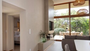 Uma sala de estar moderna com um sofá, uma mesa de centro e uma janela grande com vista para vegetação.