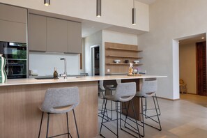 A modern kitchen with a central island, bar stools, and built-in shelves.