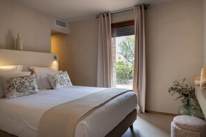 Habitación de hotel con una cama grande, una mesita de noche, un florero con flores y vistas al exterior.