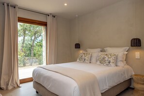 Ein Schlafzimmer mit einem groĂen Bett, Blick auf BĂ€ume durch das Fenster und einer hĂ€ngenden Leuchte.