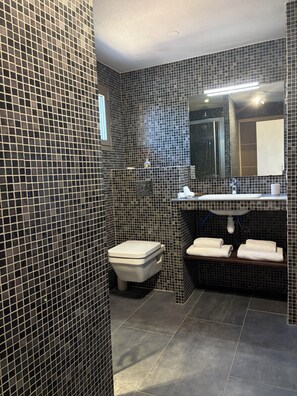 A bathroom with a tiled wall, a toilet, a sink with a mirror, and two towels on a shelf.
