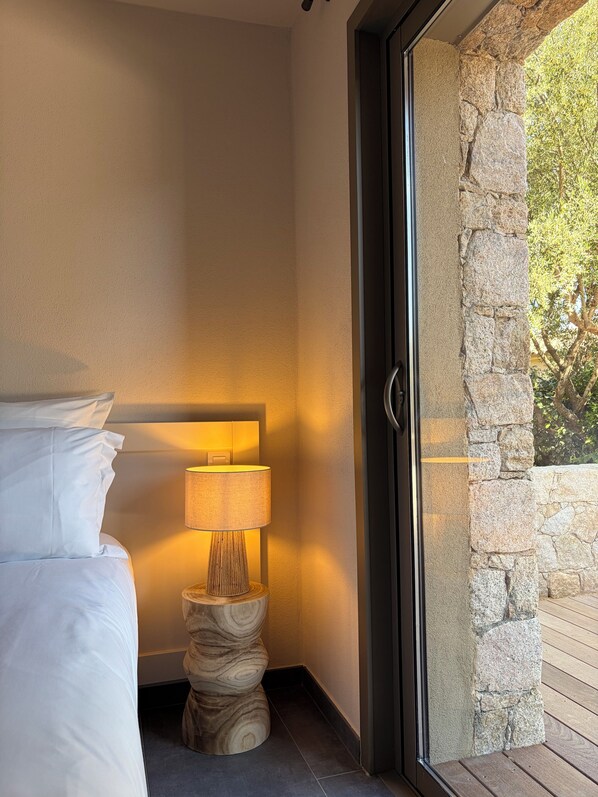 A bedroom with a bed, a lamp, and a view of the outdoors through a glass door.