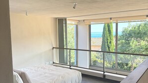 A modern bedroom with a large bed, a balcony with a railing, and a view of the sea. - Villa with swimming pool, near Lozari beach – Corsica (BELGODÈRE)