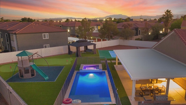 Un jardin avec une piscine, un espace de jeux et une terrasse couverte.