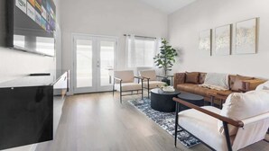 Un salon moderne avec un canapé, des fauteuils, une table basse et un téléviseur fixé au mur.
