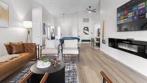 Un salon moderne comprenant un canapé, des fauteuils, une table basse, une cheminée et un téléviseur fixé au mur, qui diffuse différents services de streaming.