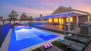 Une piscine avec un patio couvert, des chaises longues et un barbecue.