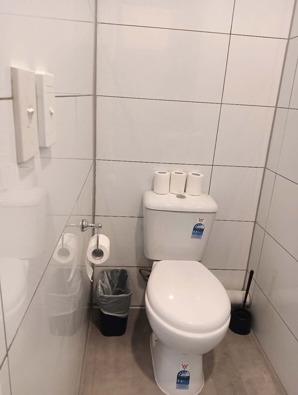 Un baño pequeño y limpio con inodoro, un cubo de basura y un dispensador de papel higiénico.