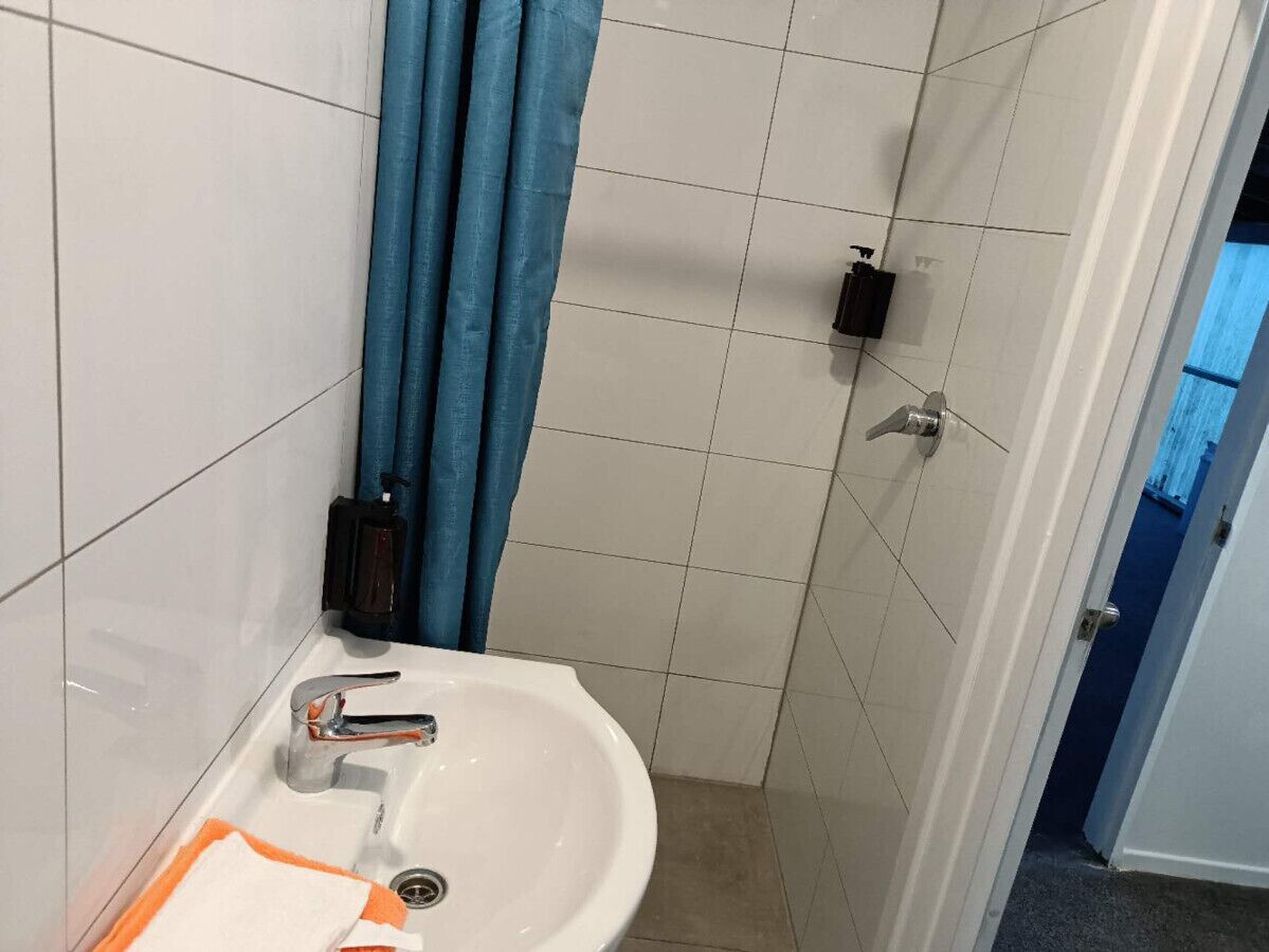 Un baño con lavamanos blanco, cortina de ducha azul y paredes con azulejos.