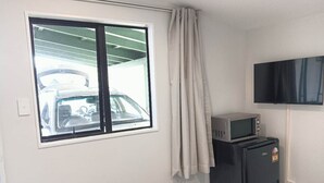 Una habitación pequeña con ventana, televisor, microondas y refrigerador.