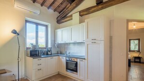 Eine Küche mit weißen Schränken, einer Mikrowelle und einem Backofen. Ein Fenster lässt Tageslicht herein und eine Stehlampe sorgt für zusätzliche Beleuchtung.
