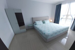 A bedroom with a bed, a wardrobe, a small table, and a window with curtains. - Lush Lakeside - Citra Luxury Apartments (Jakarta)