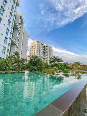 A modern residential building complex with a clear blue sky and a swimming pool in the foreground. - Lush Lakeside - Citra Luxury Apartments (Jakarta)