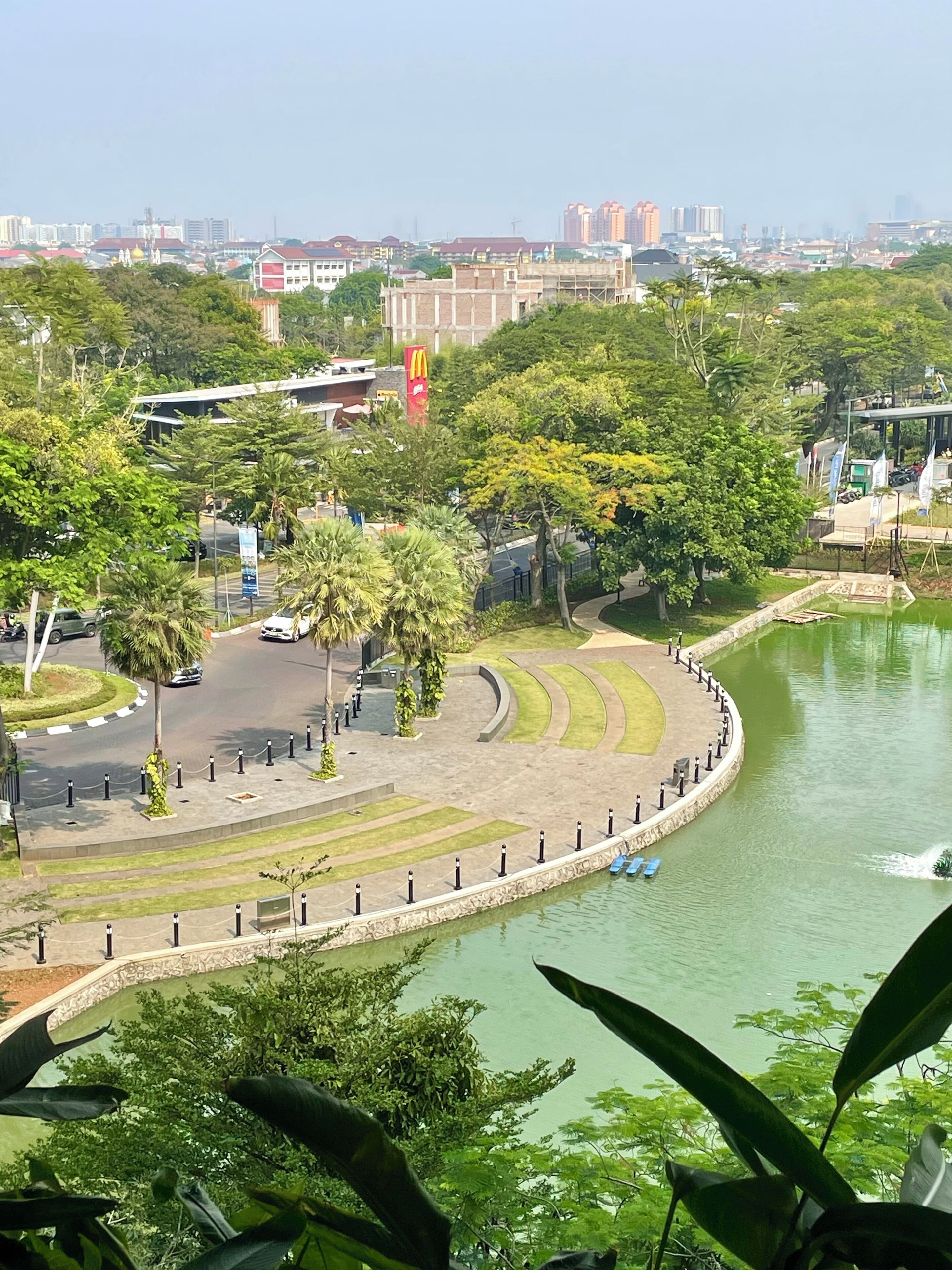 A riverside park with a curved walkway, trees, and a McDonald's restaurant in the background.
