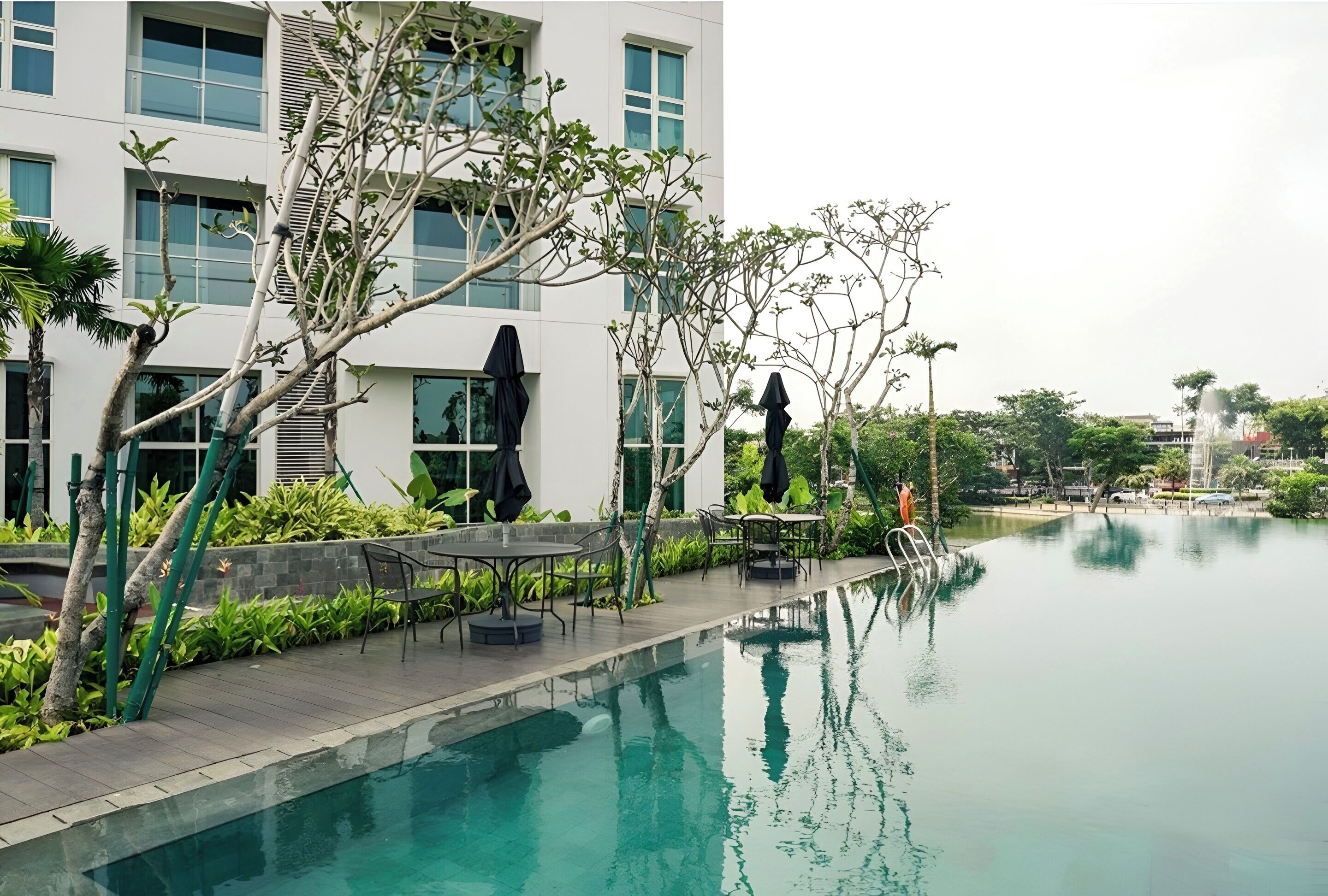 A modern building with a swimming pool, outdoor seating, and lush greenery.