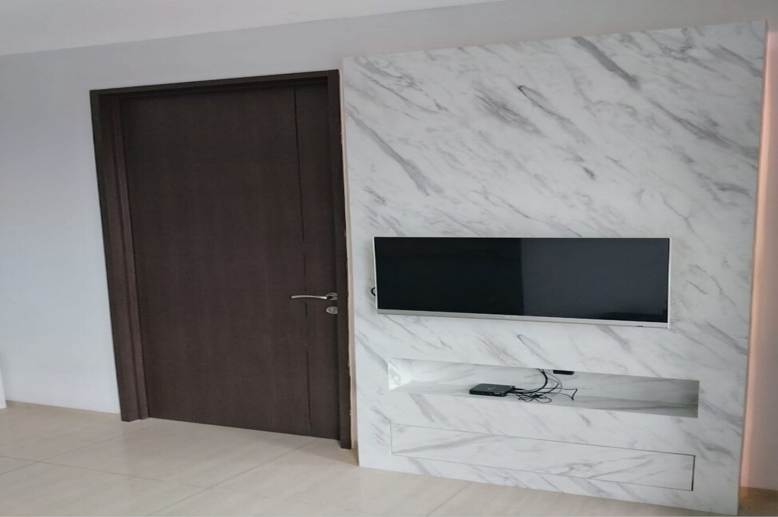 A modern room with a dark wooden door, a marble wall, and a mounted flat-screen TV.