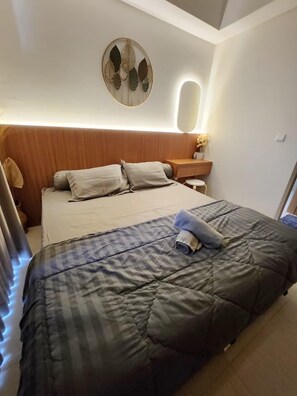 Un dormitorio moderno con una cama grande, cabecera de madera, mesita de noche con lámpara y un objeto decorativo en la pared.