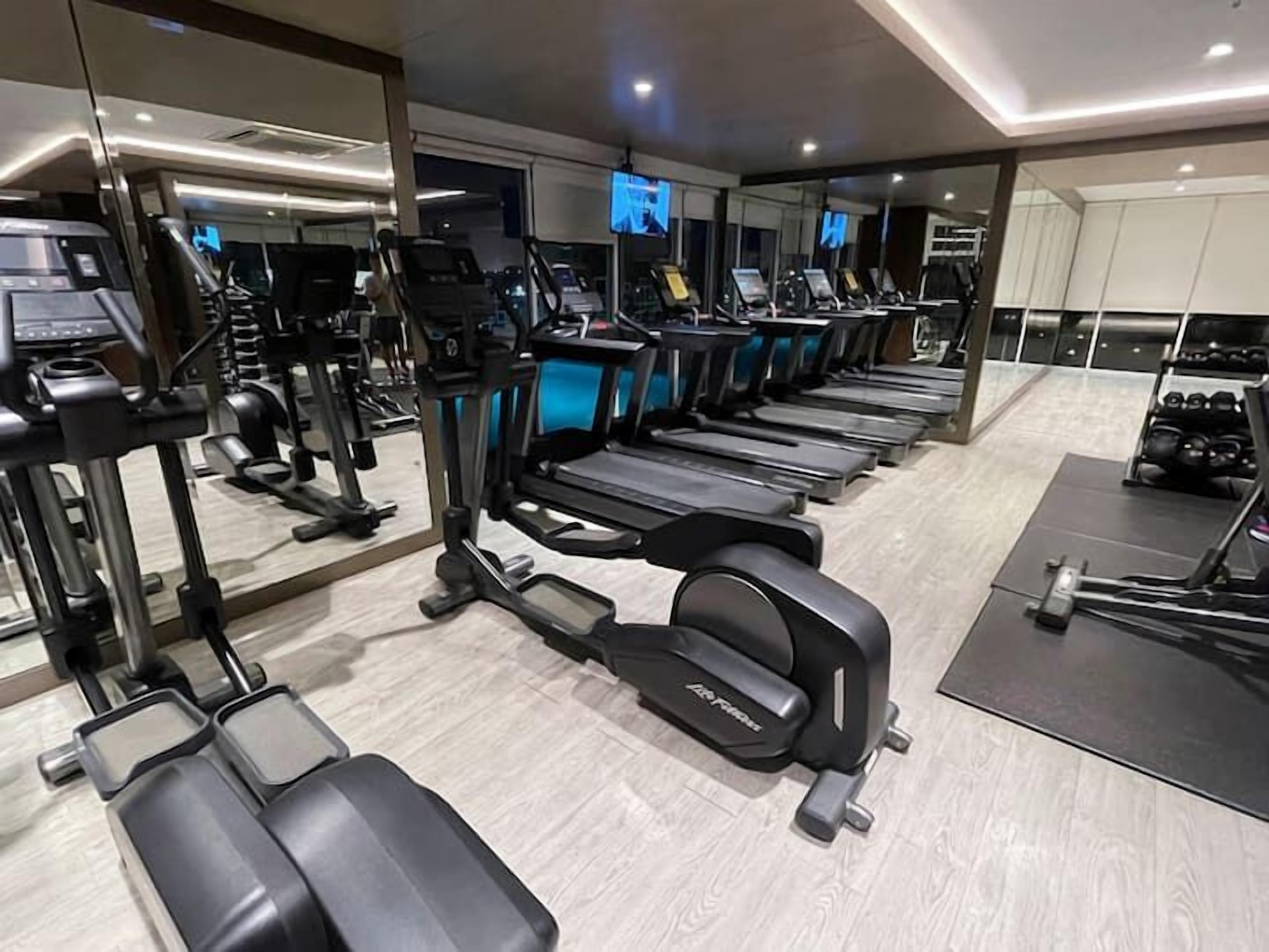 Une salle de sport équipée de plusieurs tapis de course, d’appareils de musculation et d’un mur recouvert de miroirs.