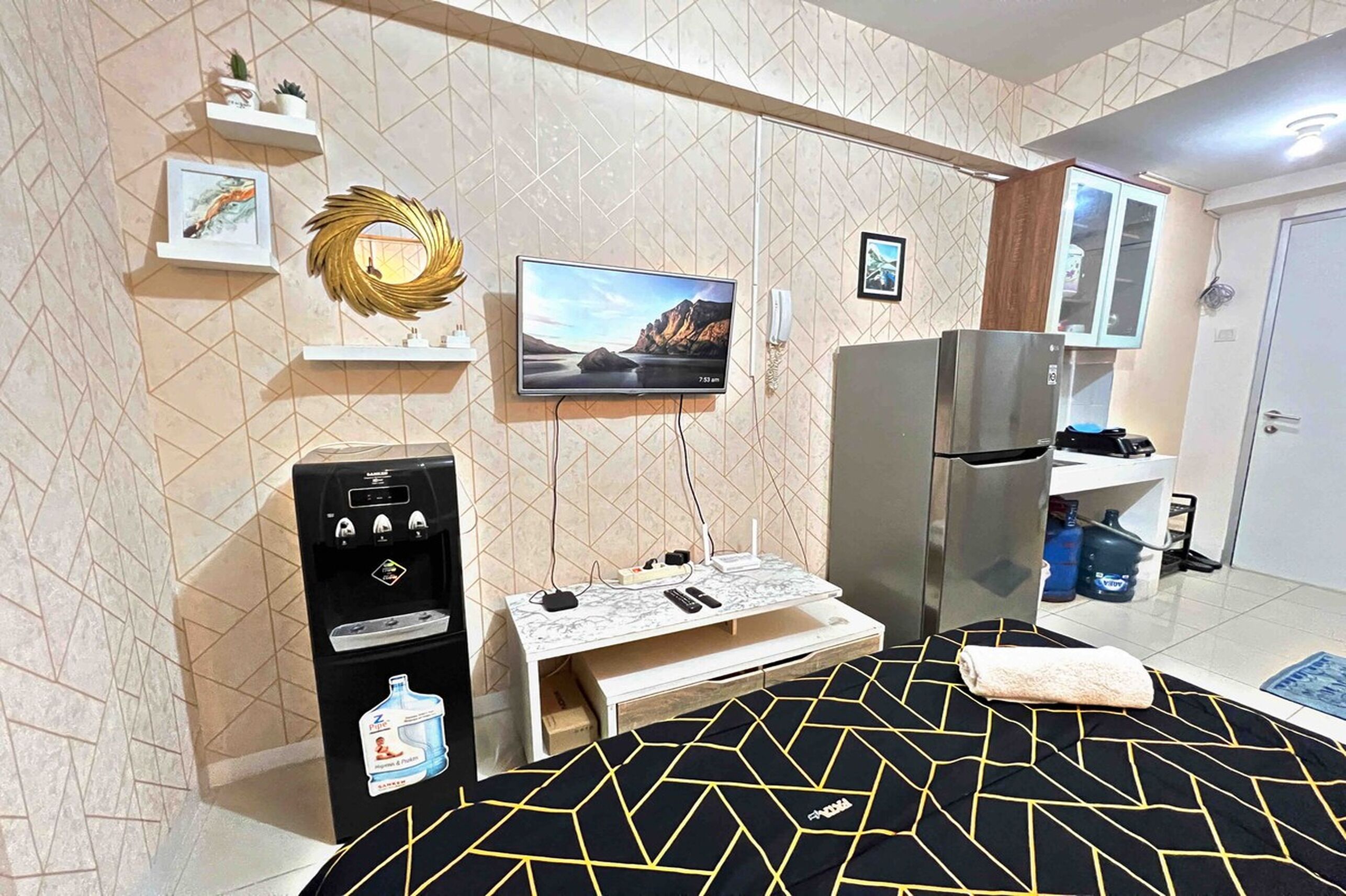 Une chambre d’hôtel compacte équipée d’un lit, d’une télévision, d’un mini-bar, d’un réfrigérateur et d’un distributeur d’eau.