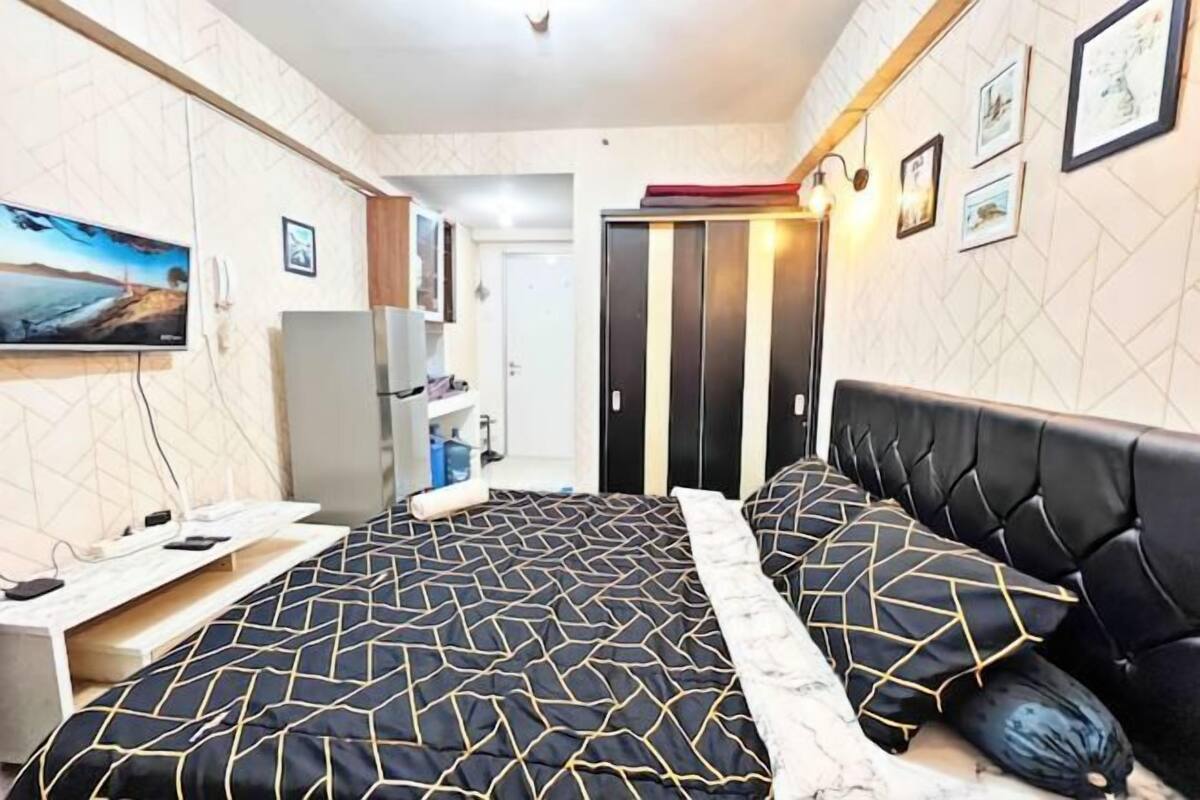 A bedroom with a bed, a desk, a wardrobe, and a TV on the wall.
