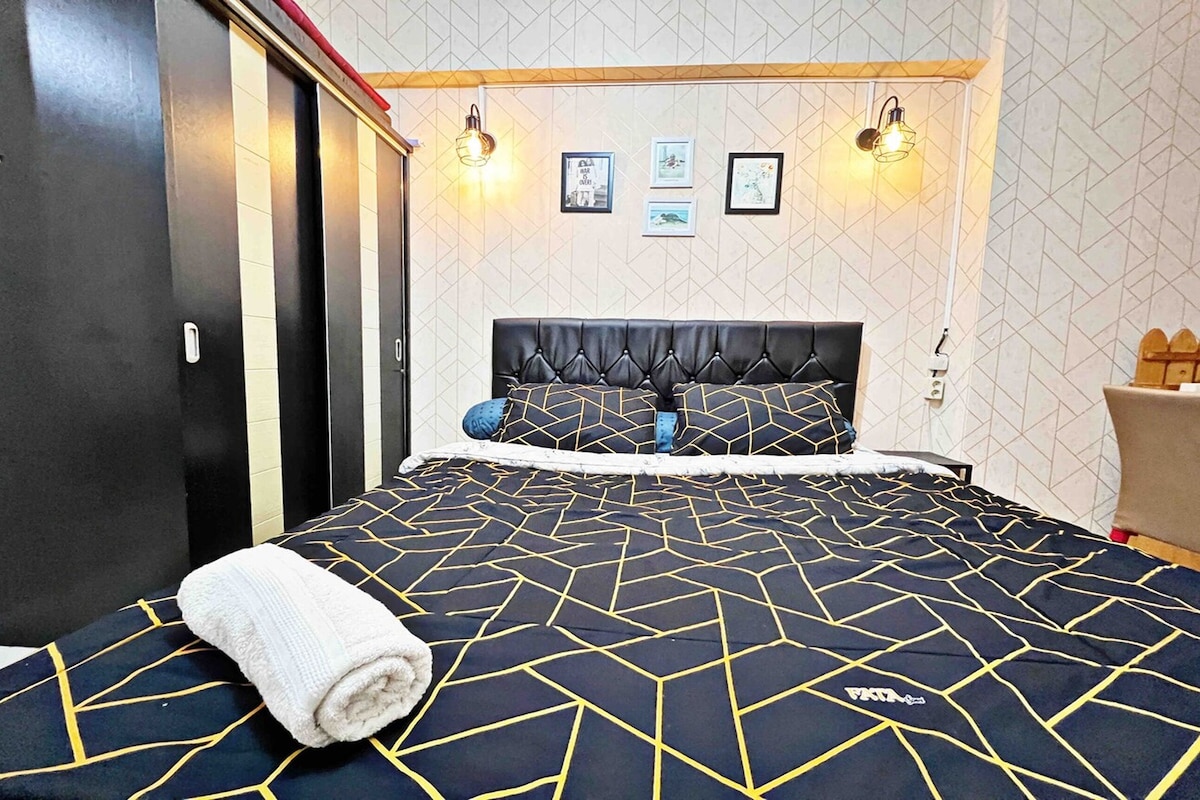 Habitación de hotel con una cama, un edredón de diseño geométrico, un cabecero capitonado y dos lámparas fijadas a la pared.