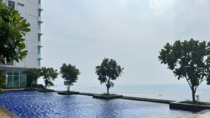 A swimming pool with a wooden deck, surrounded by trees and a view of the sea. - Sky Heaven Greenbay in North Jakarta (Jakarta)
