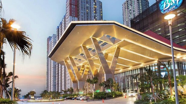 A modern building with a distinctive geometric roof structure, surrounded by high-rise buildings and palm trees. - Sky Heaven Greenbay in North Jakarta (Jakarta)