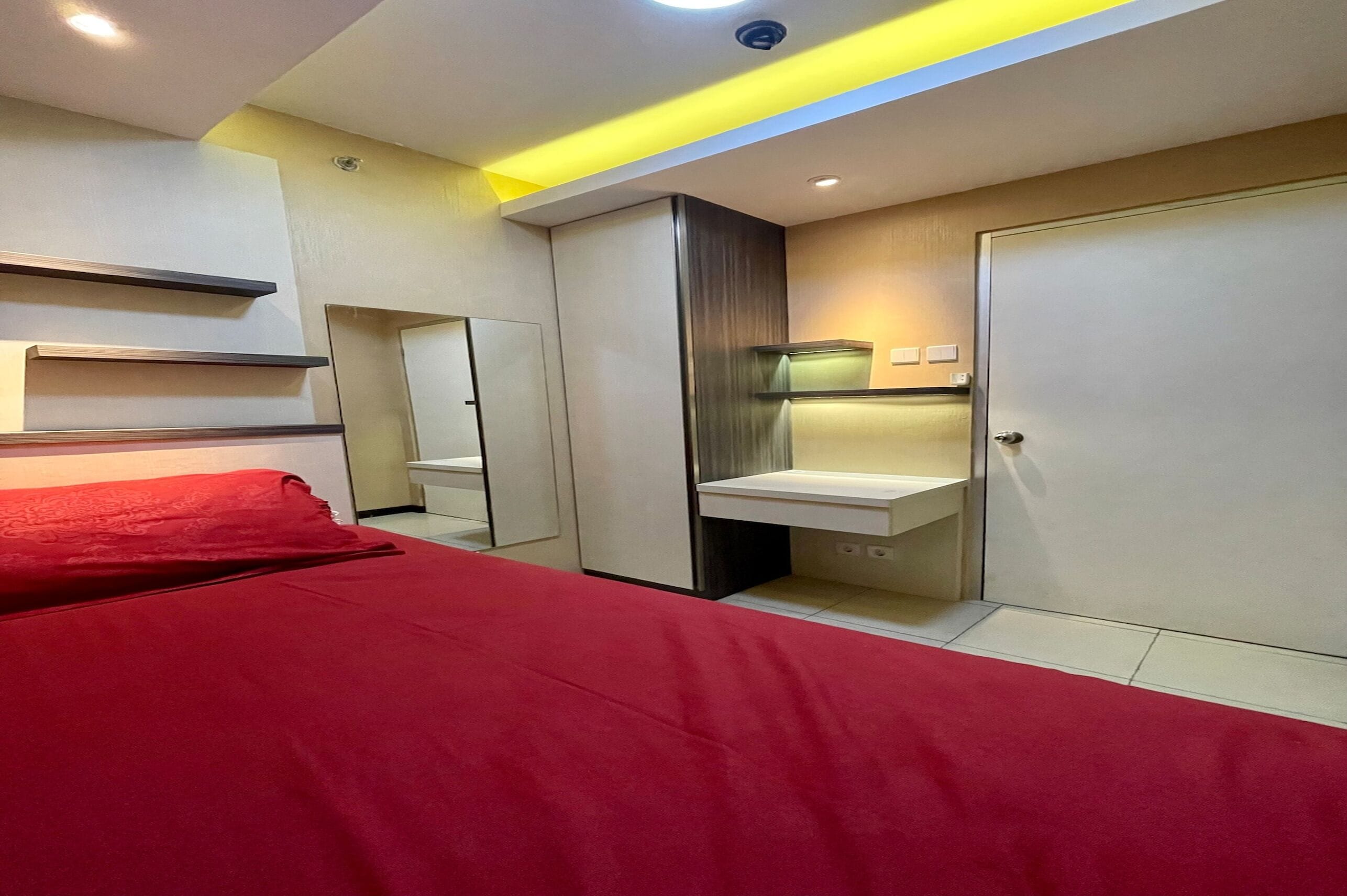 A modern bedroom with a bed, a bedside table, a mirror, a wardrobe, and a built-in sink.