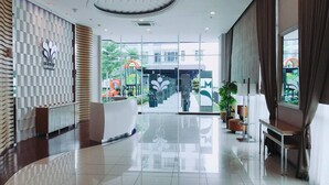 A modern hotel lobby with a reception desk, seating area, and large windows offering views of the outdoor area. - Sky Heaven Greenbay in North Jakarta (Jakarta)