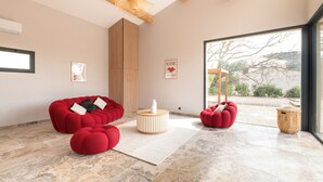 A modern living room with red furniture, a wooden ceiling, and a large window with a view of the outdoors. - Villa with pool, outdoor bar and balinese bed (Cadenet)