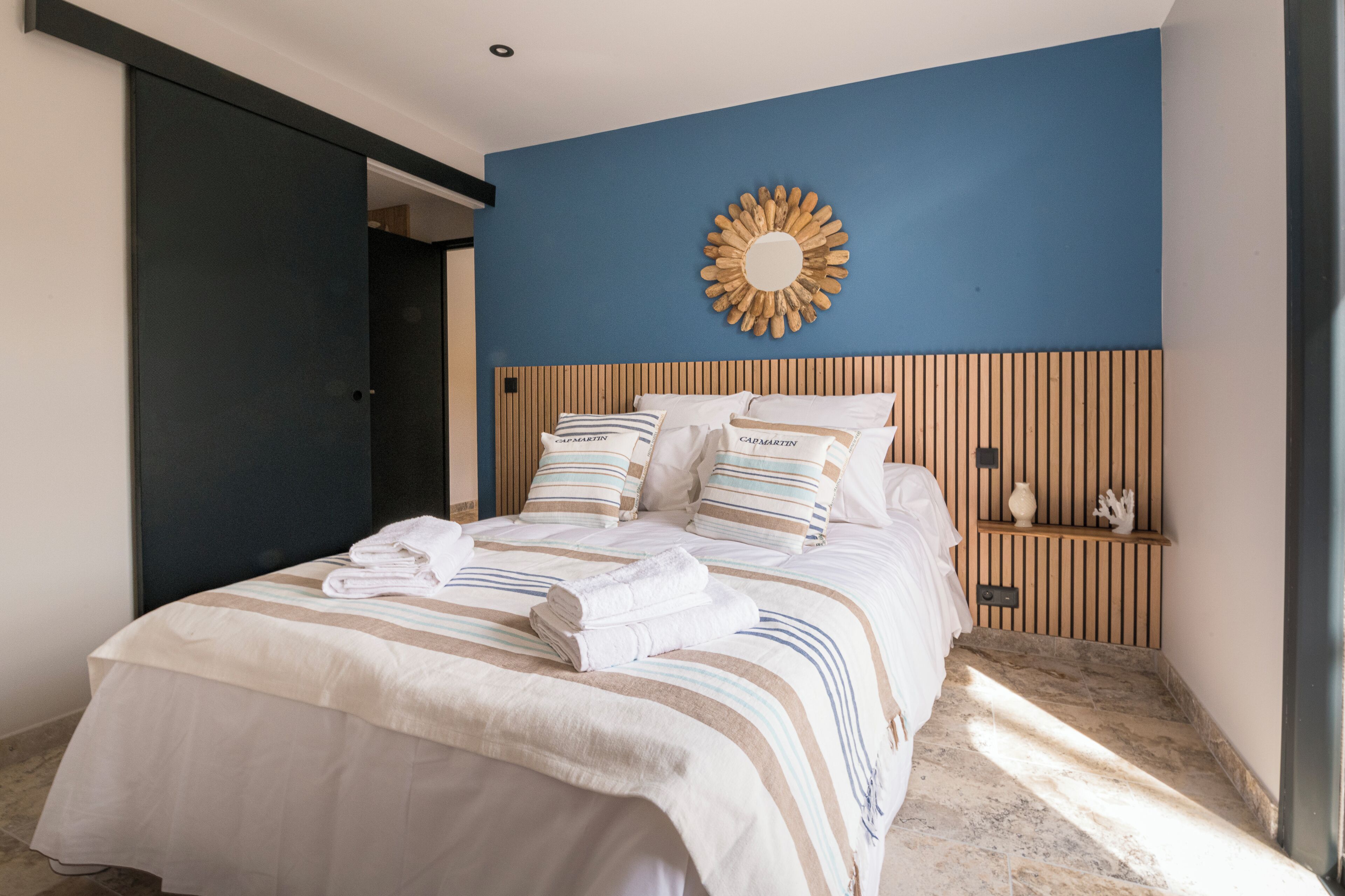 A bedroom with a bed, pillows, a nightstand, a decorative mirror, and a door.