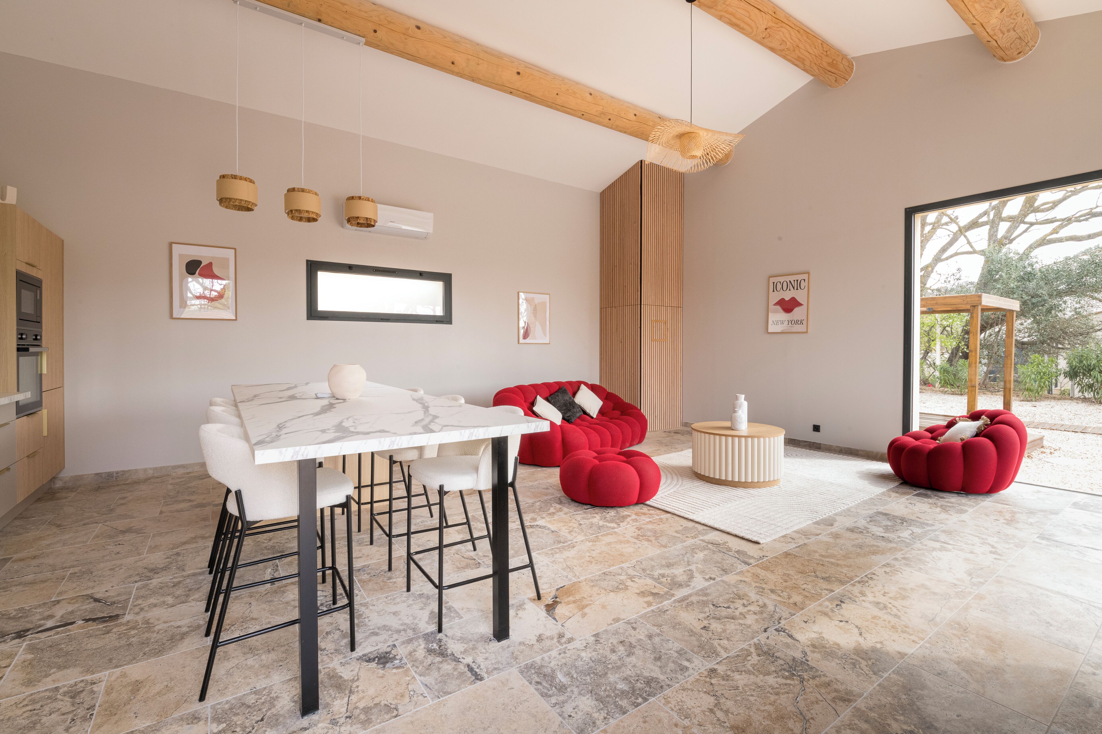 Ein modernes Interieur mit einem Esstisch aus Marmor, roten Sitzsäcken und einem großen Fenster mit Blick ins Freie.