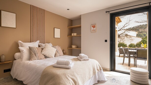 A bedroom with a large bed, bedside tables, a built-in shelf unit, and a sliding glass door leading to an outdoor seating area. - Villa with pool, outdoor bar and balinese bed (Cadenet)