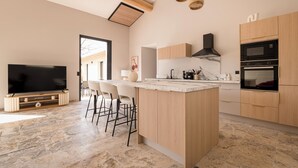 A modern kitchen with a central island, built-in appliances, and a flat-screen TV. - Villa with pool, outdoor bar and balinese bed (Cadenet)