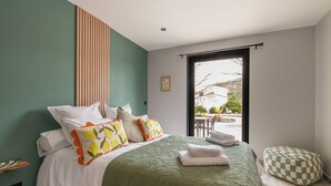 A bedroom with a bed, pillows, a green blanket, a checkered ottoman, and a view of an outdoor area. - Villa with pool, outdoor bar and balinese bed (Cadenet)