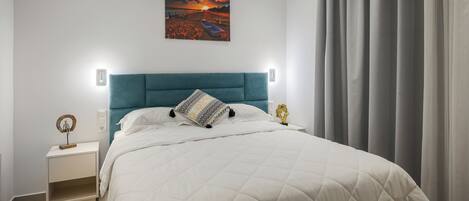 Een slaapkamer met een bed, een nachtkastje, een aan de muur hangend schilderij en een raam met gordijnen.