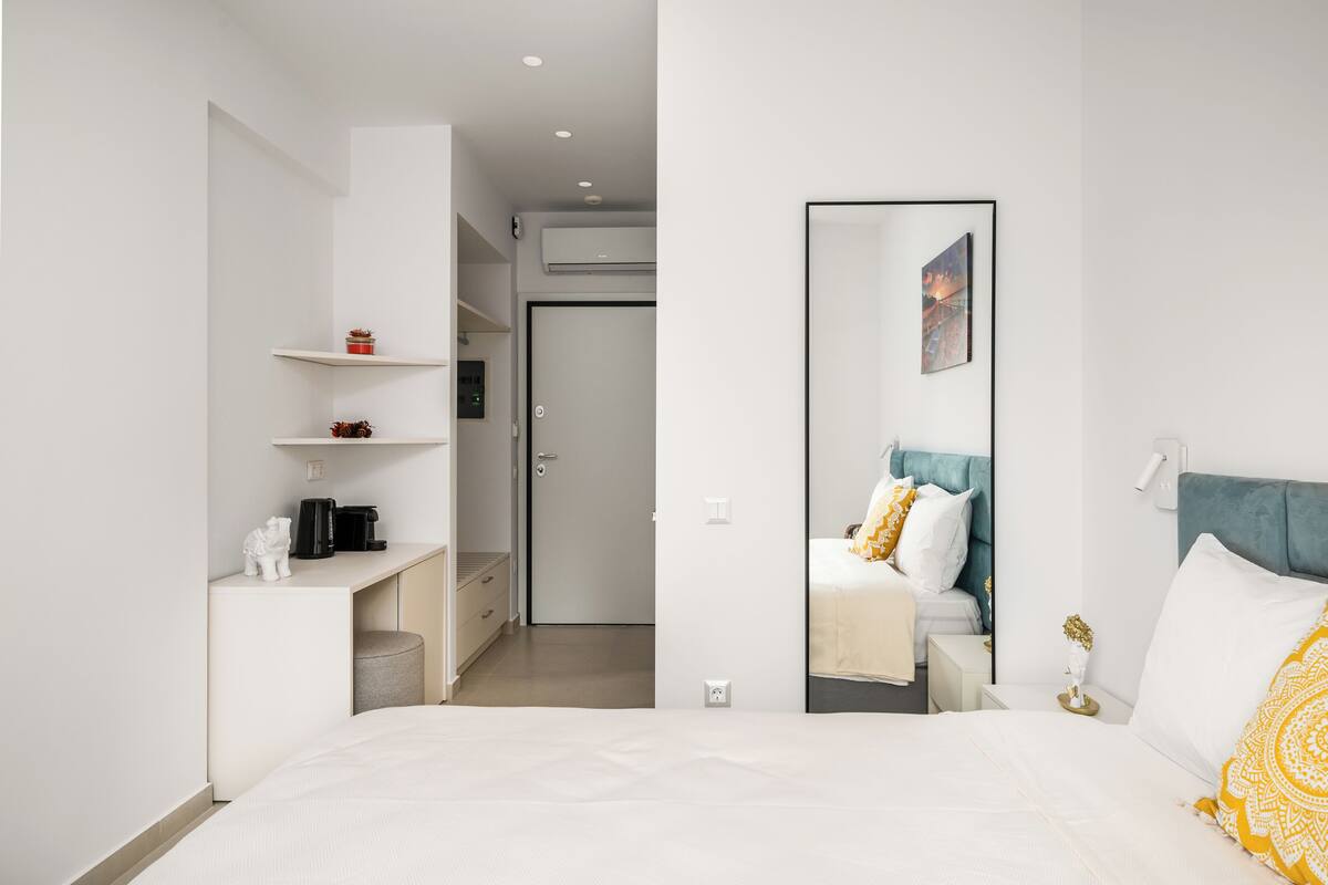 Habitació d'hotel moderna amb un llit, una taula de nit i un mirall gran. Hi ha un escriptori amb una cadira i prestatges a la part superior. L'habitació té una paleta de colors neutres.