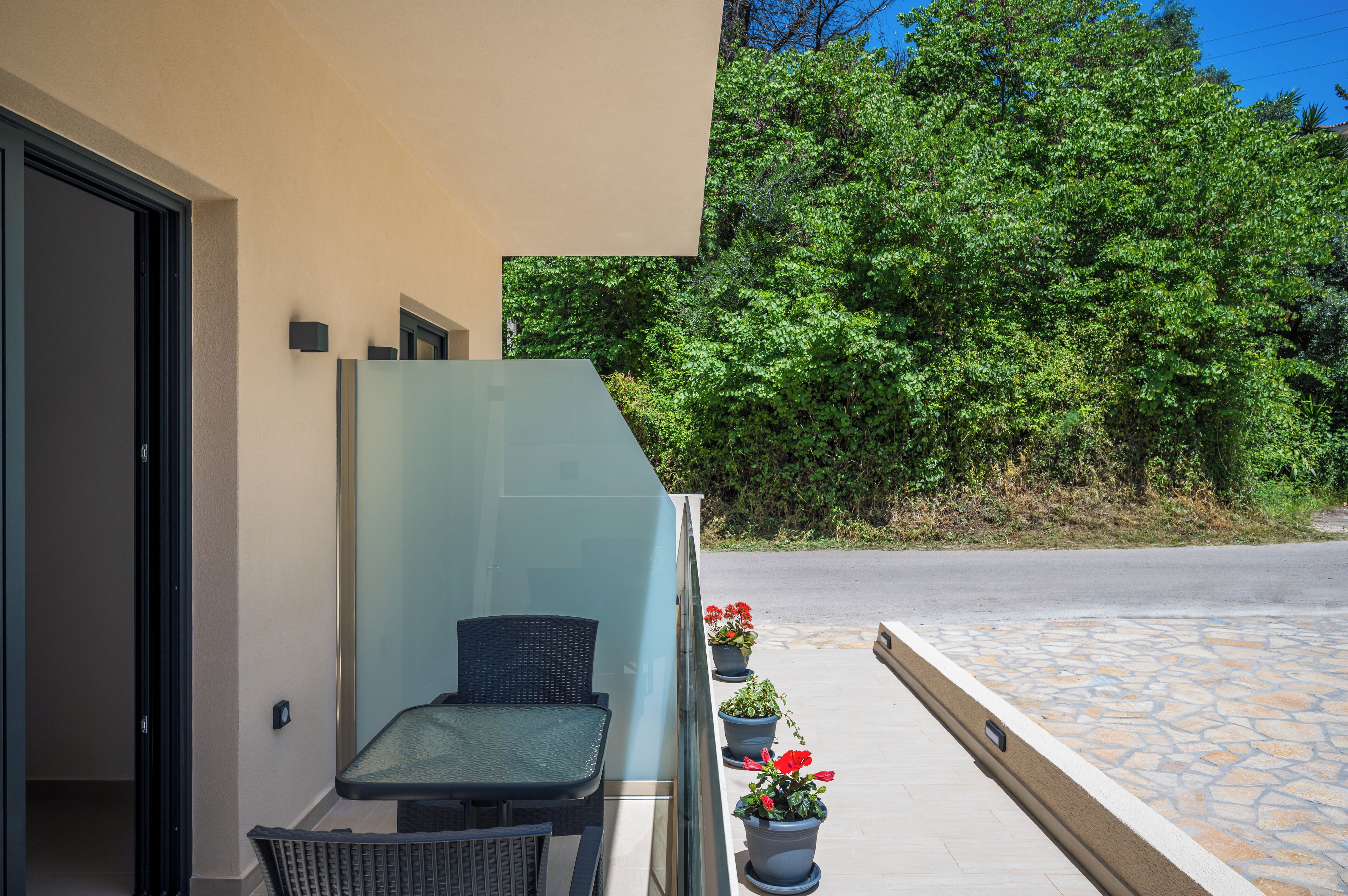 A balcony with a chair, potted plants, and a view of a road and greenery.